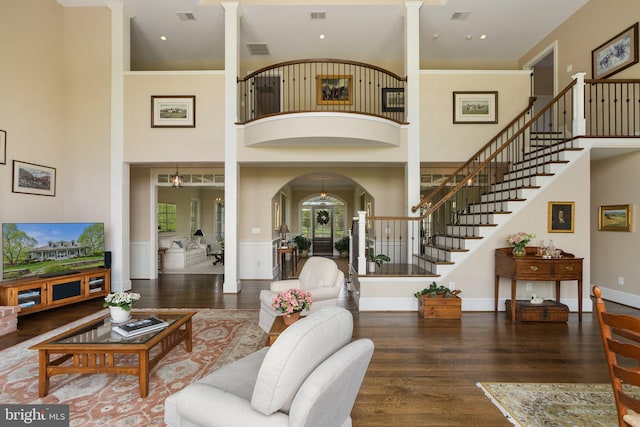living room featuring ornate columns, stairs, wood finished floors, a towering ceiling, and arched walkways