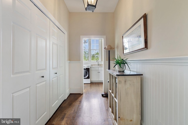 hallway with washer / clothes dryer, a wainscoted wall, a sink, and dark wood-style flooring