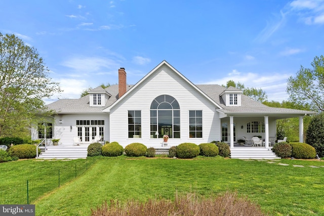 back of property featuring a yard, roof with shingles, a chimney, and covered porch