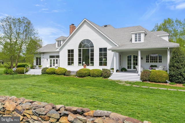rear view of property featuring french doors, a yard, roof with shingles, covered porch, and a chimney