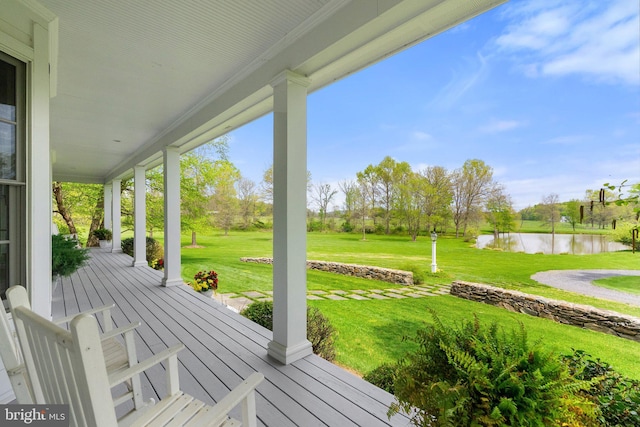 wooden terrace with a porch, a water view, and a yard