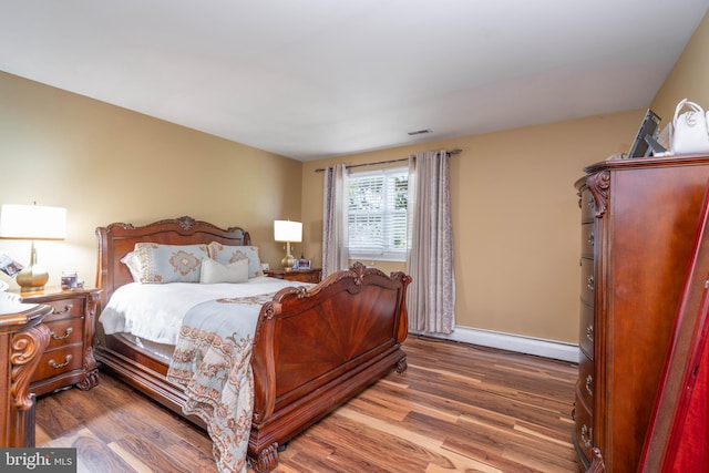 bedroom with baseboard heating, wood finished floors, and baseboards