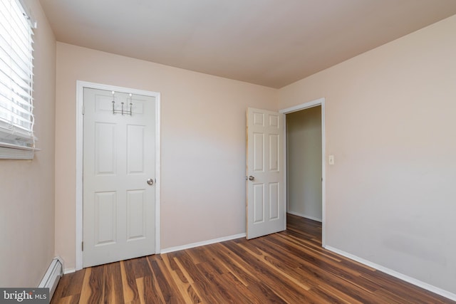unfurnished bedroom featuring a baseboard heating unit, dark wood-style flooring, and baseboards