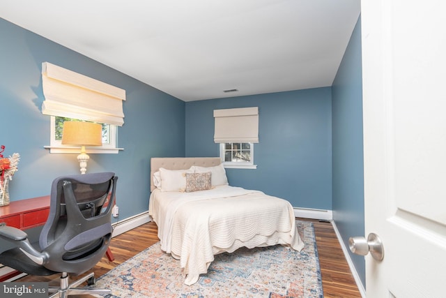 bedroom with a baseboard radiator, wood finished floors, baseboards, and an office area