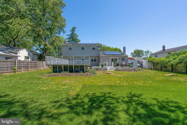 back of property with roof mounted solar panels, a chimney, a deck, and a patio