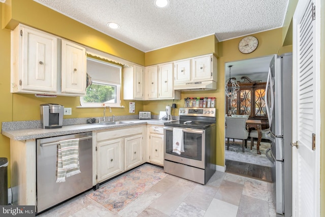 kitchen with appliances with stainless steel finishes, a sink, under cabinet range hood, a textured ceiling, and light countertops