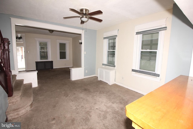 unfurnished living room with a ceiling fan, carpet, baseboards, radiator heating unit, and stairs