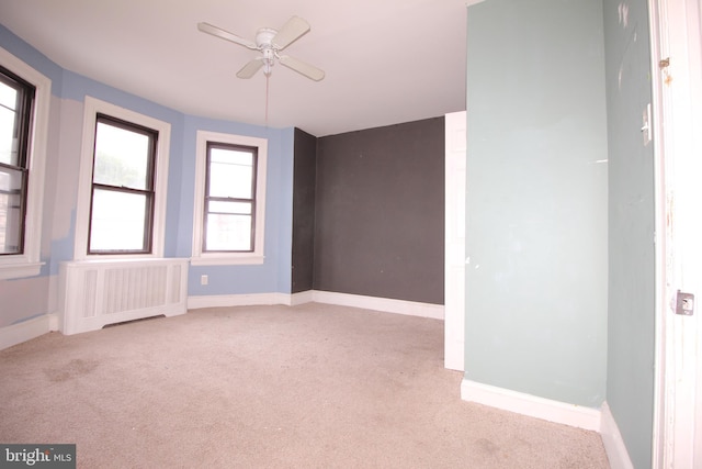 carpeted empty room with radiator, ceiling fan, and baseboards