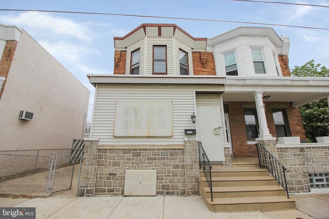 multi unit property with fence, brick siding, a porch, a gate, and stone siding
