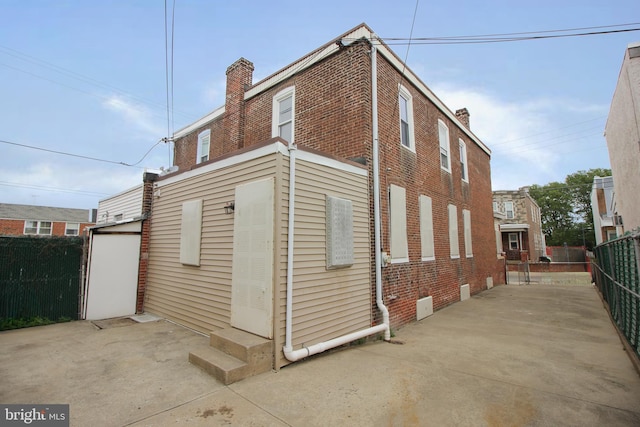 view of side of home with brick siding, fence, a chimney, and a patio area