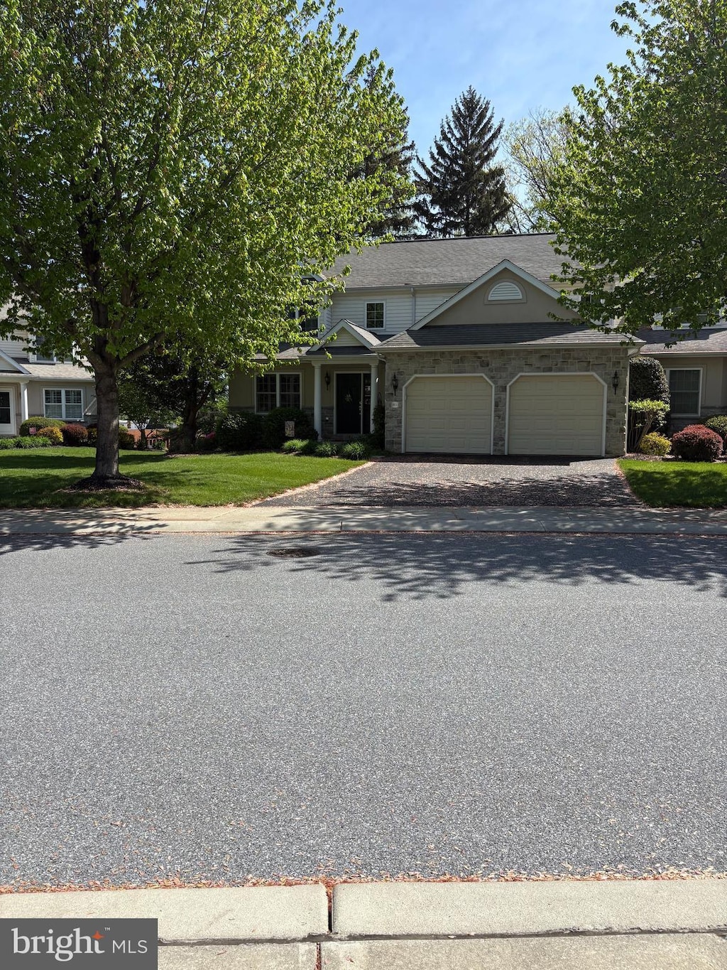view of front facade with a garage, asphalt driveway, a front lawn, and stone siding