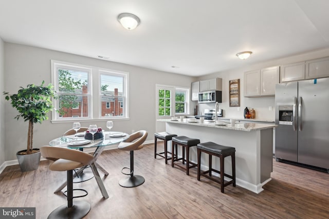 kitchen with stainless steel appliances, an island with sink, a kitchen breakfast bar, and dark wood-style floors