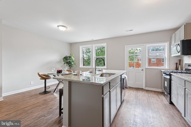 kitchen with stainless steel appliances, a sink, light wood-style floors, and baseboards