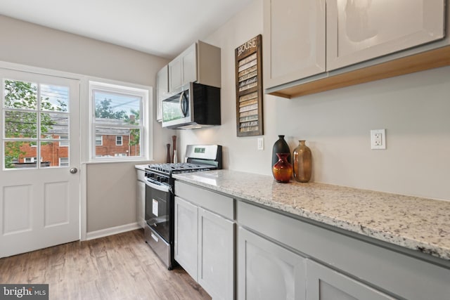 kitchen featuring appliances with stainless steel finishes, baseboards, light wood-style floors, and light stone counters