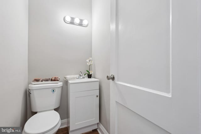 half bathroom with toilet, vanity, and baseboards