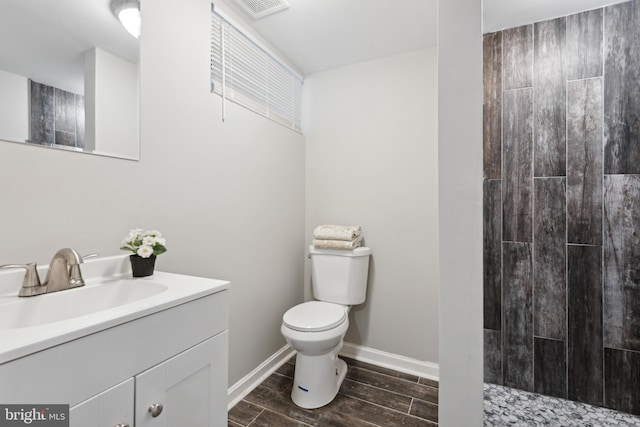 full bath featuring toilet, wood tiled floors, a tile shower, vanity, and baseboards
