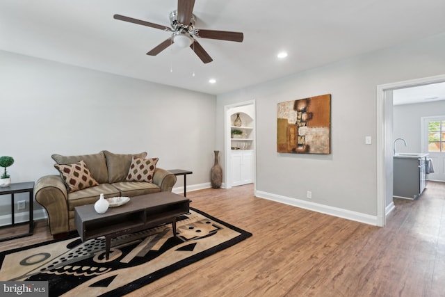 living room with light wood-type flooring, ceiling fan, baseboards, recessed lighting, and built in features