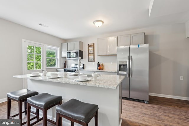 kitchen with appliances with stainless steel finishes, a center island with sink, dark wood finished floors, and baseboards