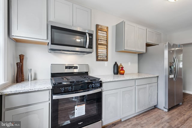 kitchen featuring stainless steel appliances, light wood-type flooring, and light stone countertops