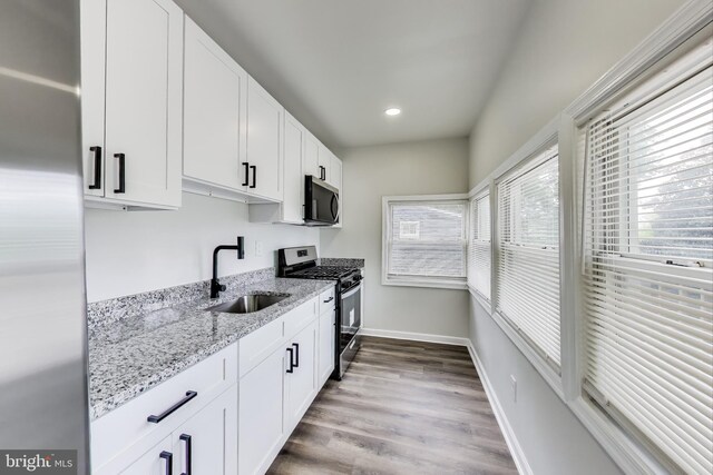 kitchen featuring appliances with stainless steel finishes, a sink, white cabinets, light stone counters, and recessed lighting