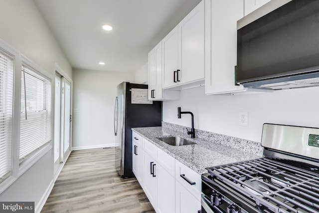 kitchen featuring stainless steel appliances, a sink, recessed lighting, light stone counters, and light wood-style floors