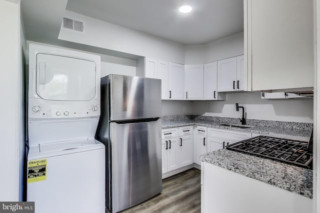 kitchen featuring freestanding refrigerator, stacked washer / dryer, a sink, white cabinets, and wood finished floors