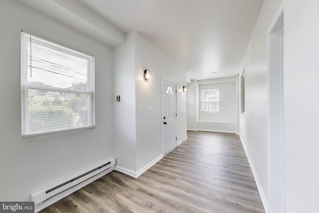 corridor featuring a baseboard radiator, plenty of natural light, wood finished floors, and baseboards