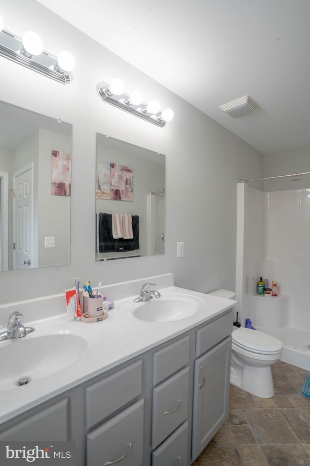 bathroom featuring a shower, toilet, double vanity, and stone finish floors