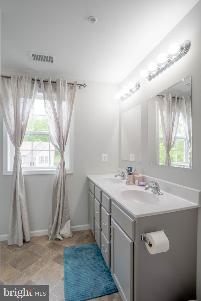 bathroom with healthy amount of natural light, double vanity, baseboards, and stone finish floors