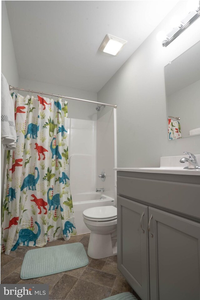 full bath featuring toilet, vanity, shower / bath combination with curtain, and stone finish flooring