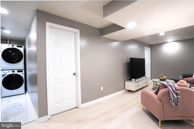 living area featuring estacked washer and dryer, baseboards, and light wood finished floors