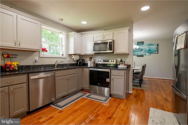 kitchen featuring appliances with stainless steel finishes, a sink, light wood-type flooring, decorative light fixtures, and white cabinets