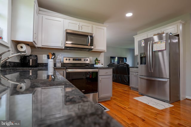 kitchen featuring appliances with stainless steel finishes, white cabinetry, light wood-style flooring, recessed lighting, and dark stone countertops