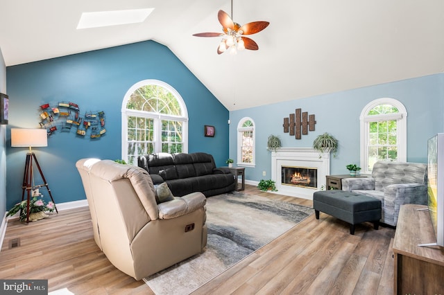 living area with a skylight, a ceiling fan, wood finished floors, healthy amount of natural light, and high vaulted ceiling