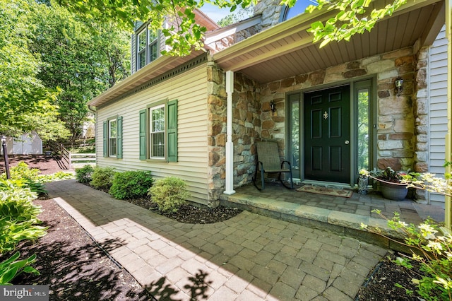 view of exterior entry with stone siding and covered porch