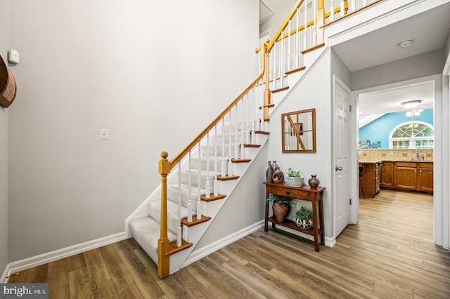 stairway with wood finished floors, ceiling fan, baseboards, and vaulted ceiling