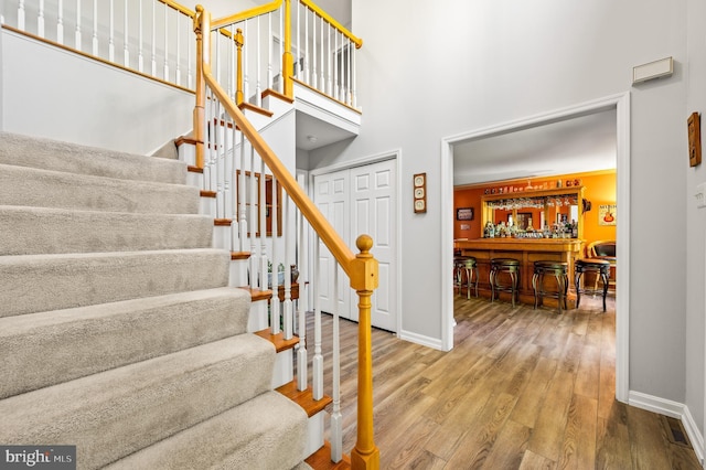 stairway featuring a bar, baseboards, wood finished floors, and a towering ceiling