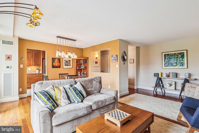 living room featuring a textured ceiling, light wood-type flooring, and baseboards