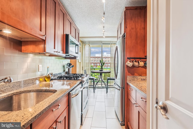 kitchen featuring appliances with stainless steel finishes, track lighting, tasteful backsplash, a sink, and light stone countertops