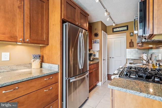kitchen featuring freestanding refrigerator, a sink, brown cabinetry, decorative backsplash, and light stone counters