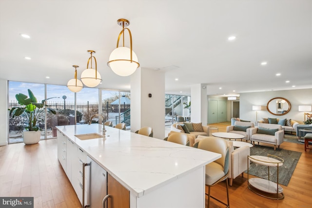 kitchen featuring a sink, light wood-type flooring, a center island with sink, recessed lighting, and decorative light fixtures