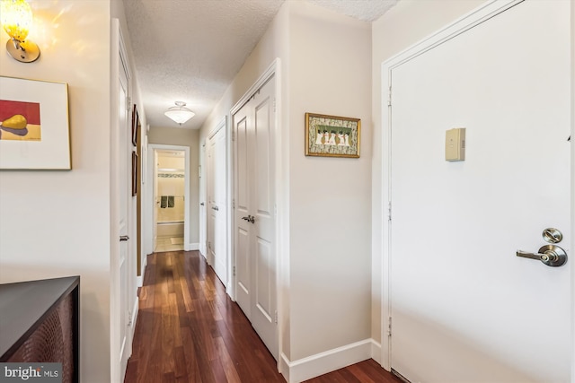hallway featuring a textured ceiling, dark wood-type flooring, and baseboards