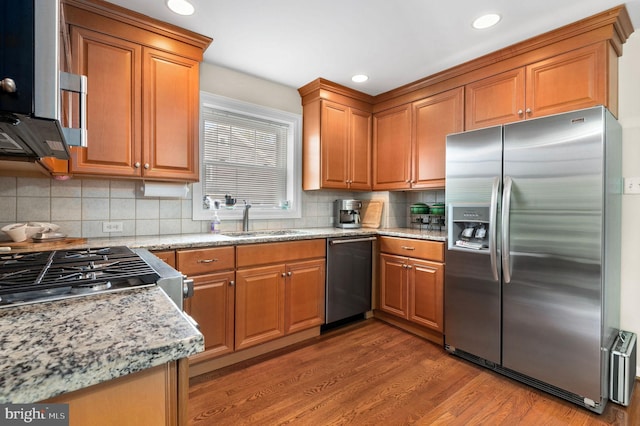 kitchen with stainless steel appliances, a sink, brown cabinets, light wood finished floors, and backsplash