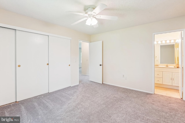 unfurnished bedroom featuring carpet flooring, a closet, a sink, connected bathroom, and a ceiling fan