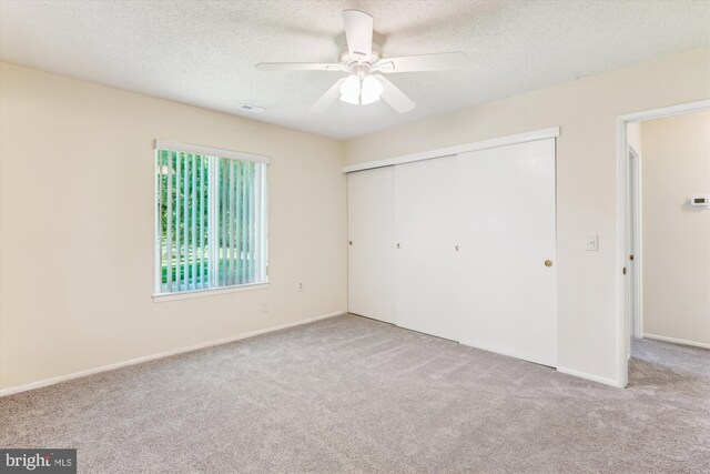 unfurnished bedroom featuring carpet, a closet, a textured ceiling, baseboards, and ceiling fan