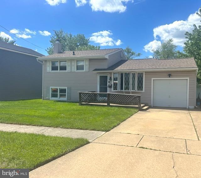 tri-level home with a garage, a chimney, a front yard, and driveway