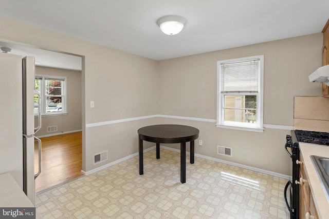 kitchen featuring black range with gas cooktop, ventilation hood, baseboards, freestanding refrigerator, and light countertops