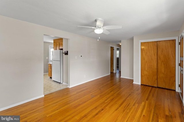 unfurnished bedroom featuring freestanding refrigerator, light wood-style flooring, baseboards, and a closet