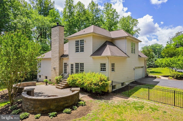 back of house with asphalt driveway, a garage, a chimney, and a shingled roof