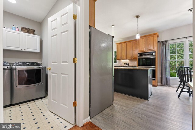 kitchen with stainless steel appliances, washer and clothes dryer, a center island, light wood finished floors, and hanging light fixtures
